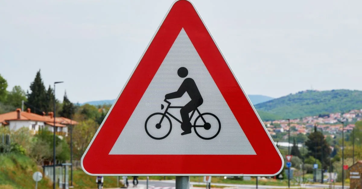 Panneau triangulaire de signalisation pour cyclistes le long d'une route rurale, indiquant la présence de cyclistes.