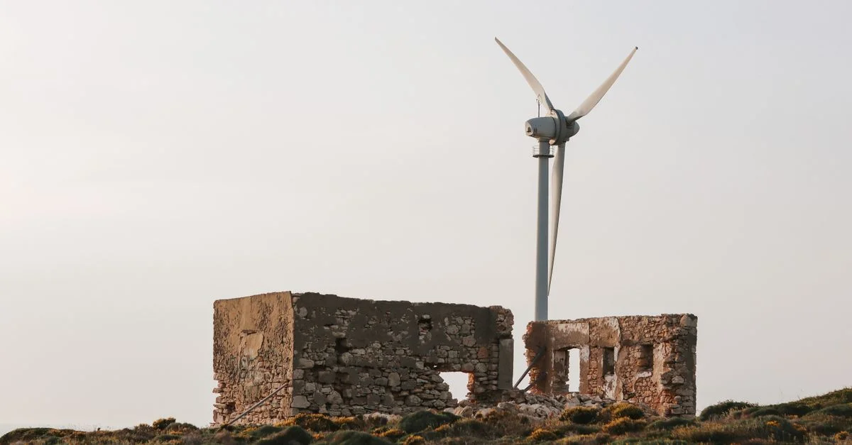 Éolienne à côté de ruines anciennes en pierre sous un ciel dégagé, symbolisant l'énergie et l'histoire.