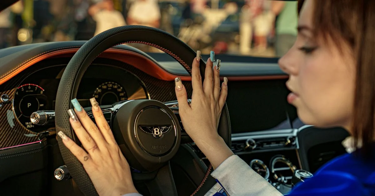 Jeune femme touchant le volant de l'intérieur d'une voiture de luxe, illustrant l'élégance et la sophistication.