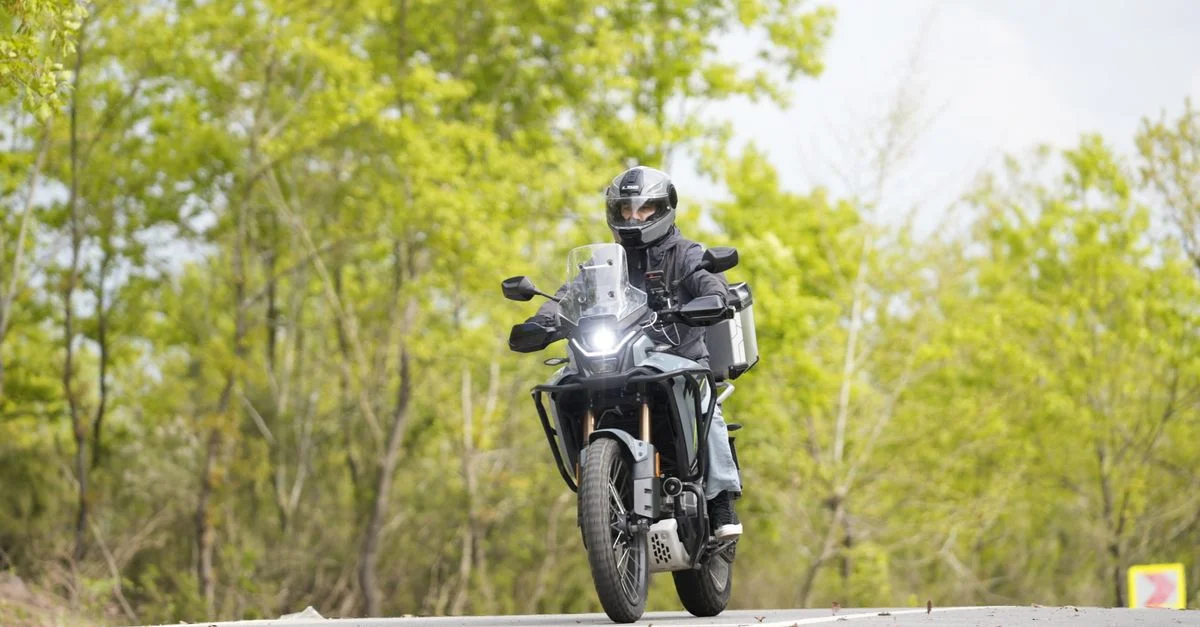 Un motard en équipement de sécurité roule sur une route forestière pittoresque en pleine journée.