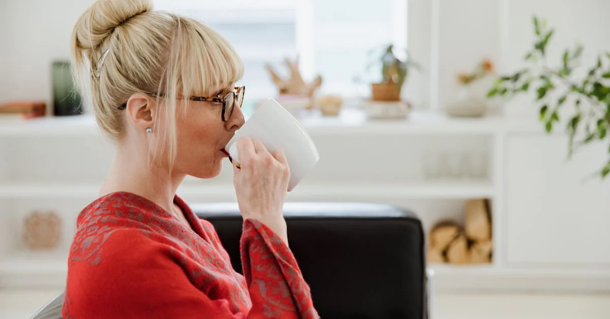 Une femme blonde élégante déguste une boisson chaude dans un salon moderne et confortable.
