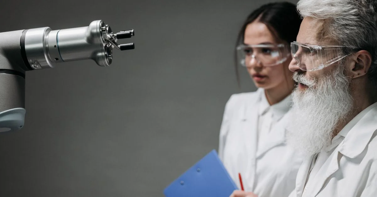 Deux scientifiques portant des blouses de laboratoire et des lunettes analysent un bras robotique dans un cadre de laboratoire.