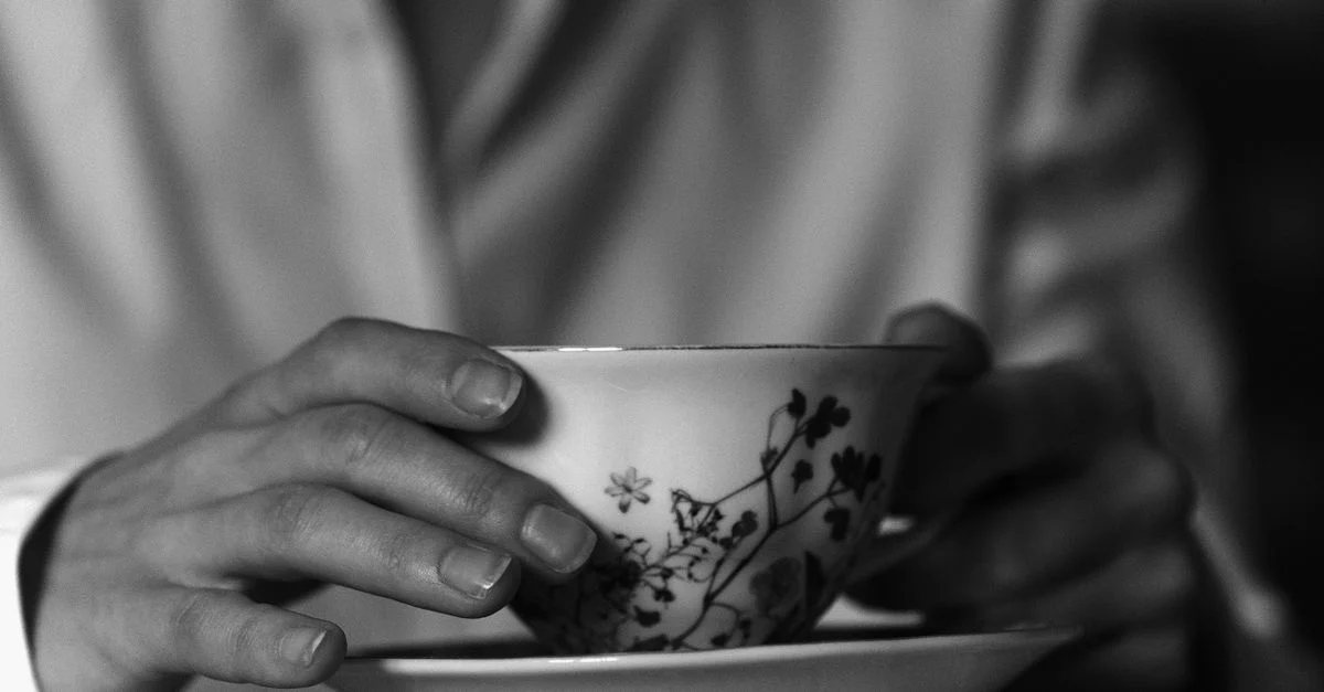 Prise de vue monochrome élégante de mains tenant une tasse au design floral.