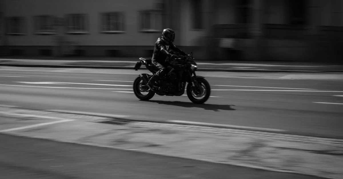 Motard parcourant les rues de la ville en noir et blanc, mettant en avant la vitesse et le mouvement.