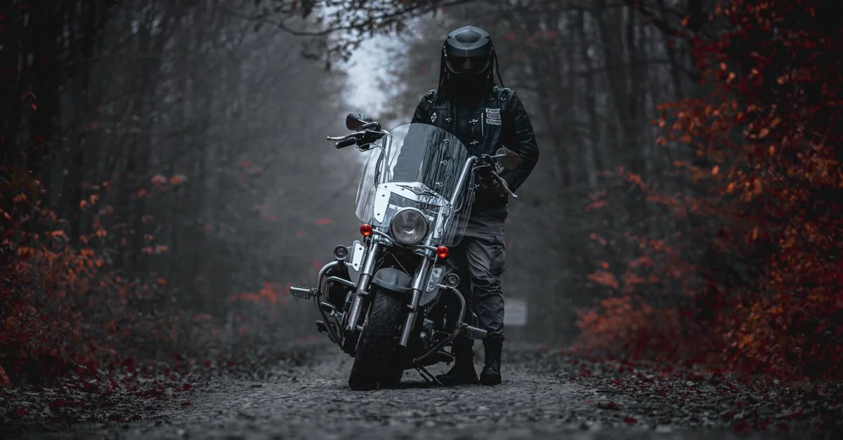 Un motard avec un casque se tient à côté d'une moto dans une forêt d'automne mystérieuse.