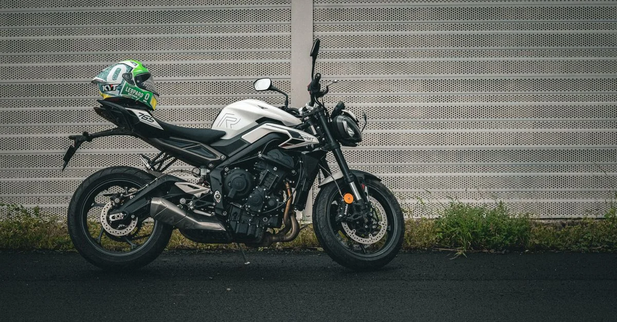 Vue latérale d'une moto sportive élégante avec un casque, garée contre un mur de grillage moderne.