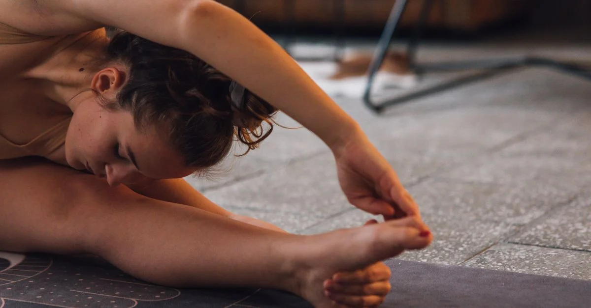 Femme s'étirant sur un tapis de yoga à l'intérieur, montrant flexibilité et concentration.