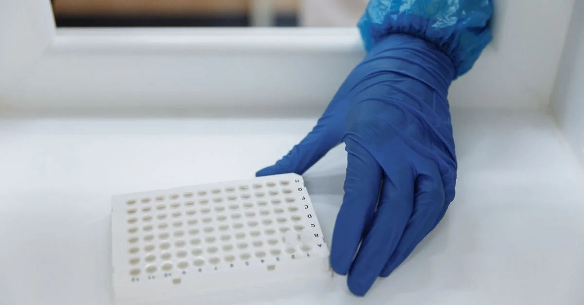 Scientifique avec des gants de protection manipulant des échantillons de test dans un environnement de laboratoire stérile.