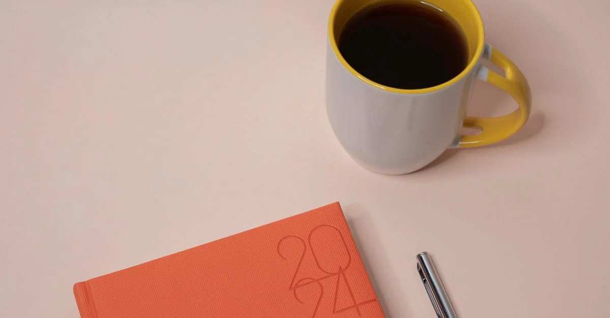 Dispositif de bureau élégant avec un planificateur 2024, une tasse de café et un stylo sur un fond clair.