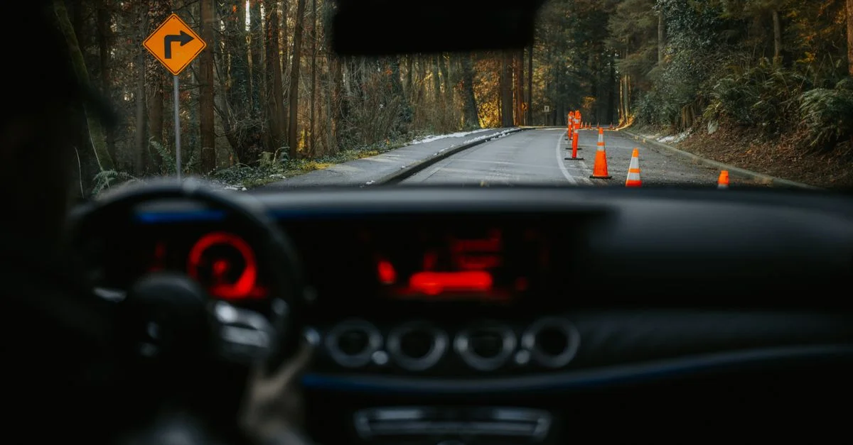 Vue depuis le tableau de bord de la voiture sur une route rurale avec des cônes de signalisation et un panneau de virage. Expérience de conduite pittoresque en forêt.