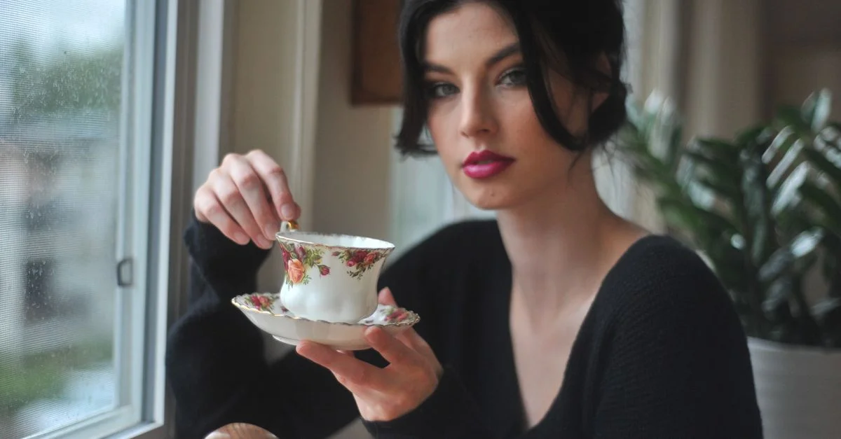 Une femme contemplative savoure du thé dans une délicate tasse à thé près de la fenêtre.